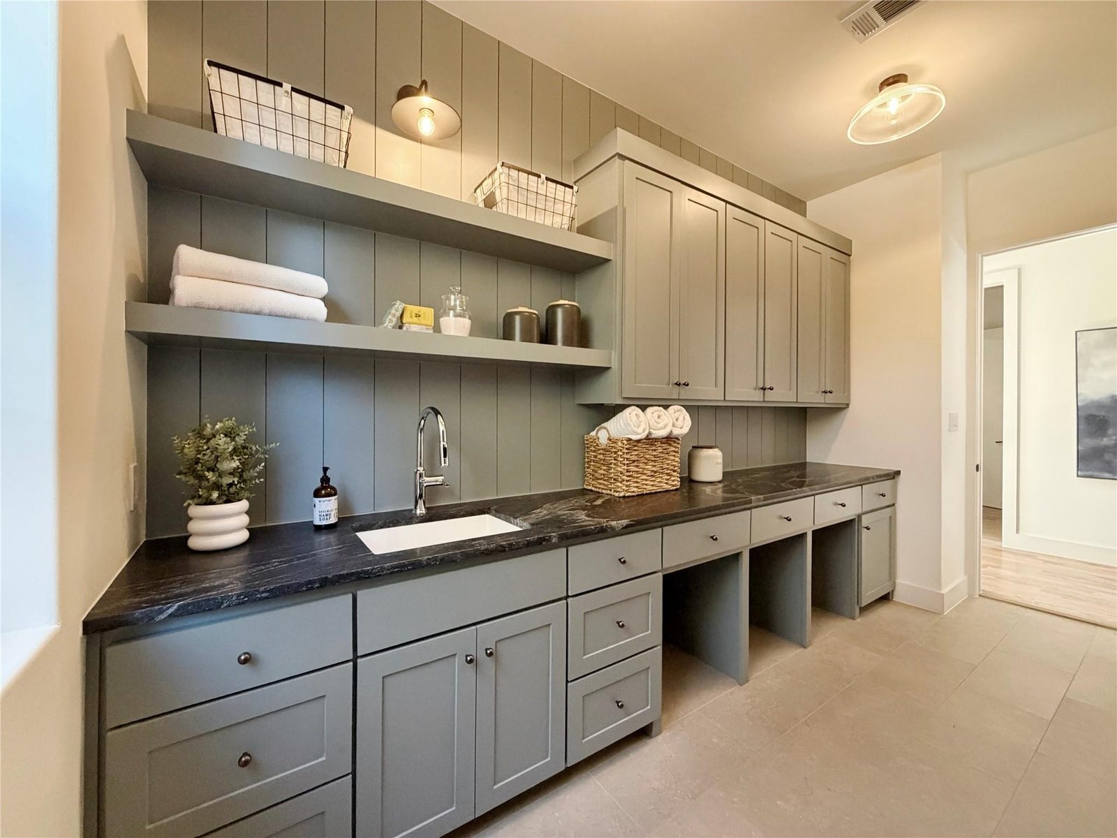 Laundry room with sage cabinetry styled with rolled towels, baskets and a plant